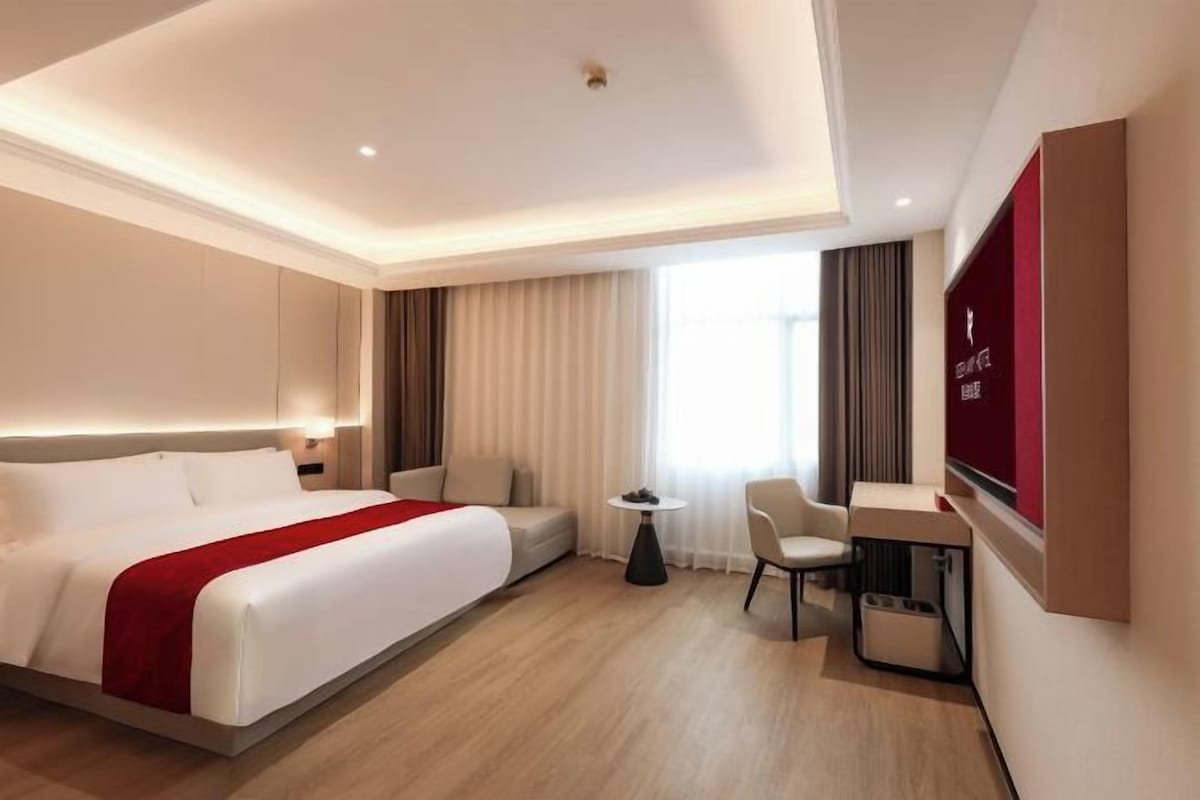 A hotel room with a large bed, a desk, a chair, and a TV.