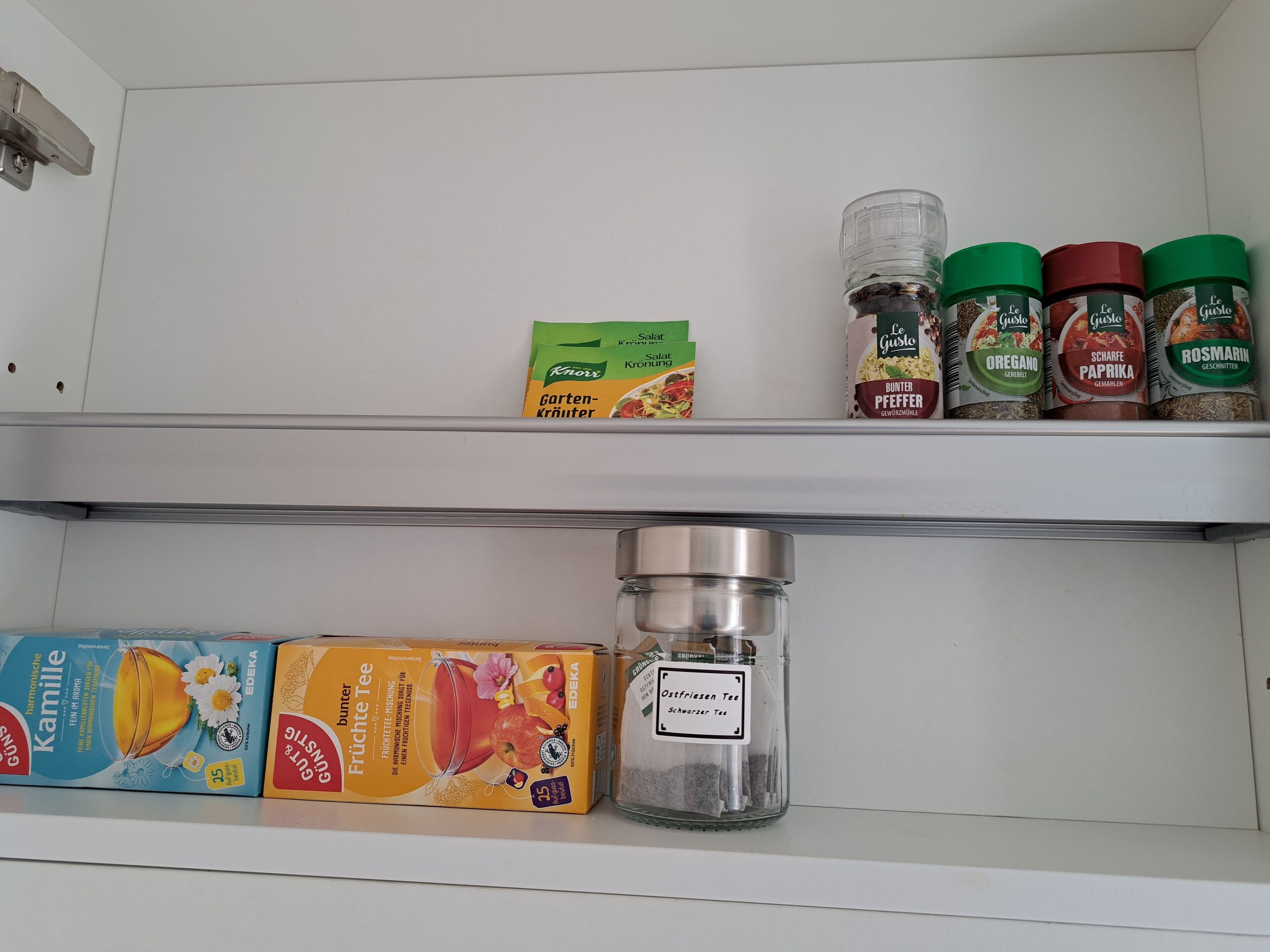 A kitchen shelf with various food items including packaged food, spices, and a container of tea.