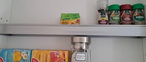 A kitchen shelf with various food items including packaged food, spices, and a container of tea.