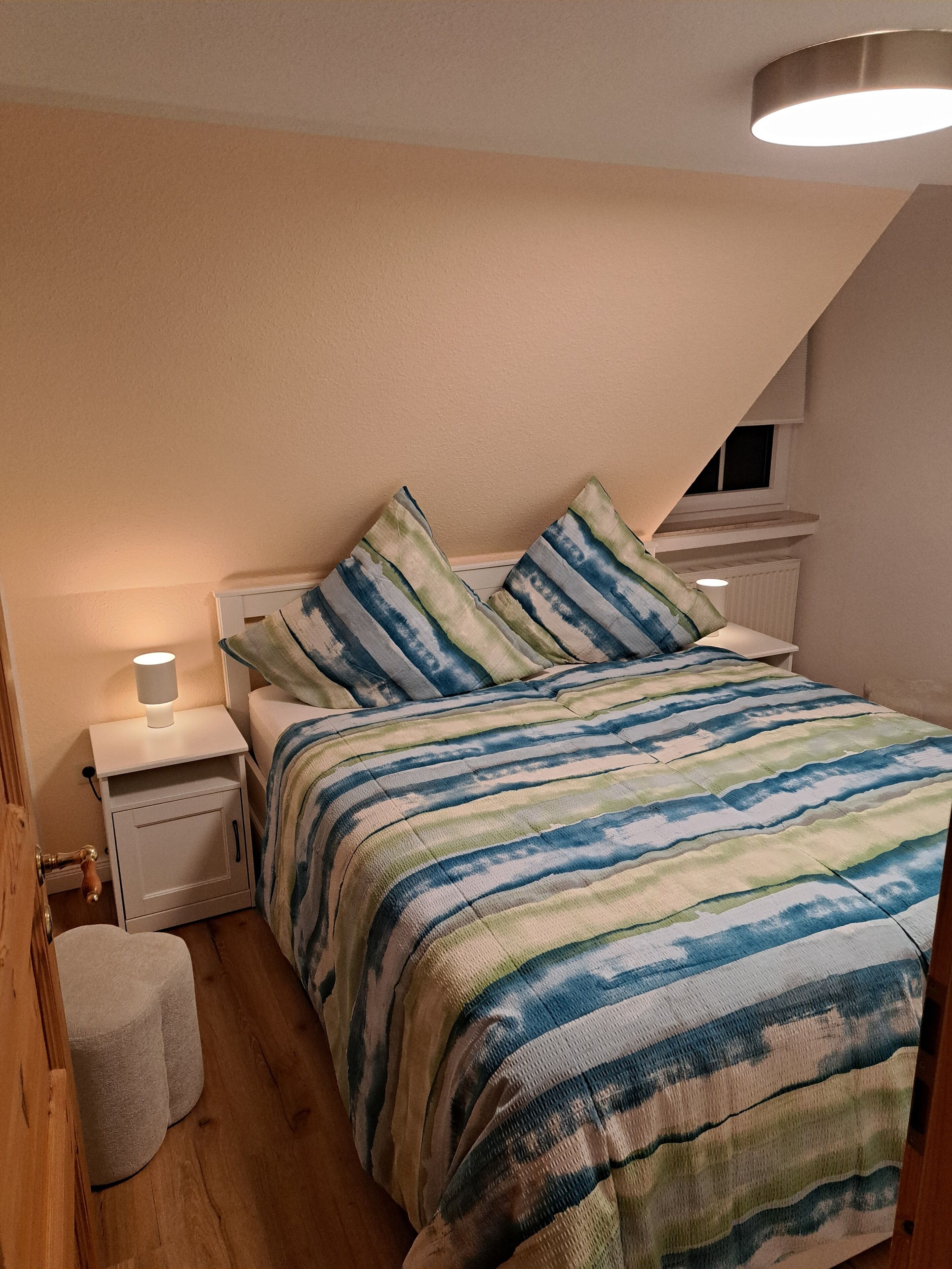 Ein Schlafzimmer mit Bett, Nachttischen, einer Lampe und einem Fenster.