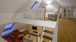 An attic bedroom with a sloped ceiling, a white picket fence, a red sofa, a small TV stand, and a wooden floor. - A millside dream, stylish, right next to the historic mill, not far from the harbor... (Ditzum)
