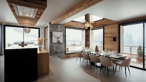 A modern dining area with a large table set for six, wooden beams on the ceiling, and a stone wall with a deer picture.