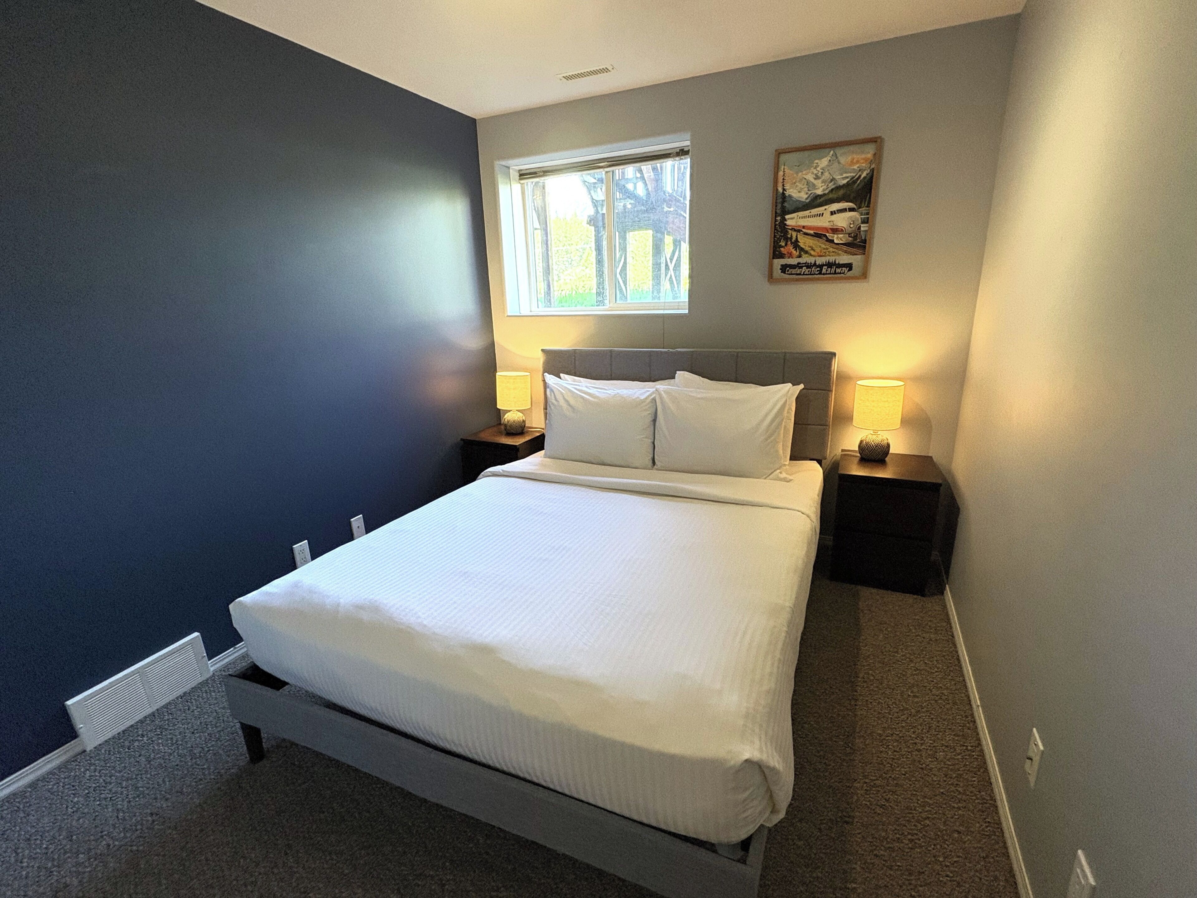 A bedroom with a bed, two bedside tables with lamps, a window, and a poster on the wall.