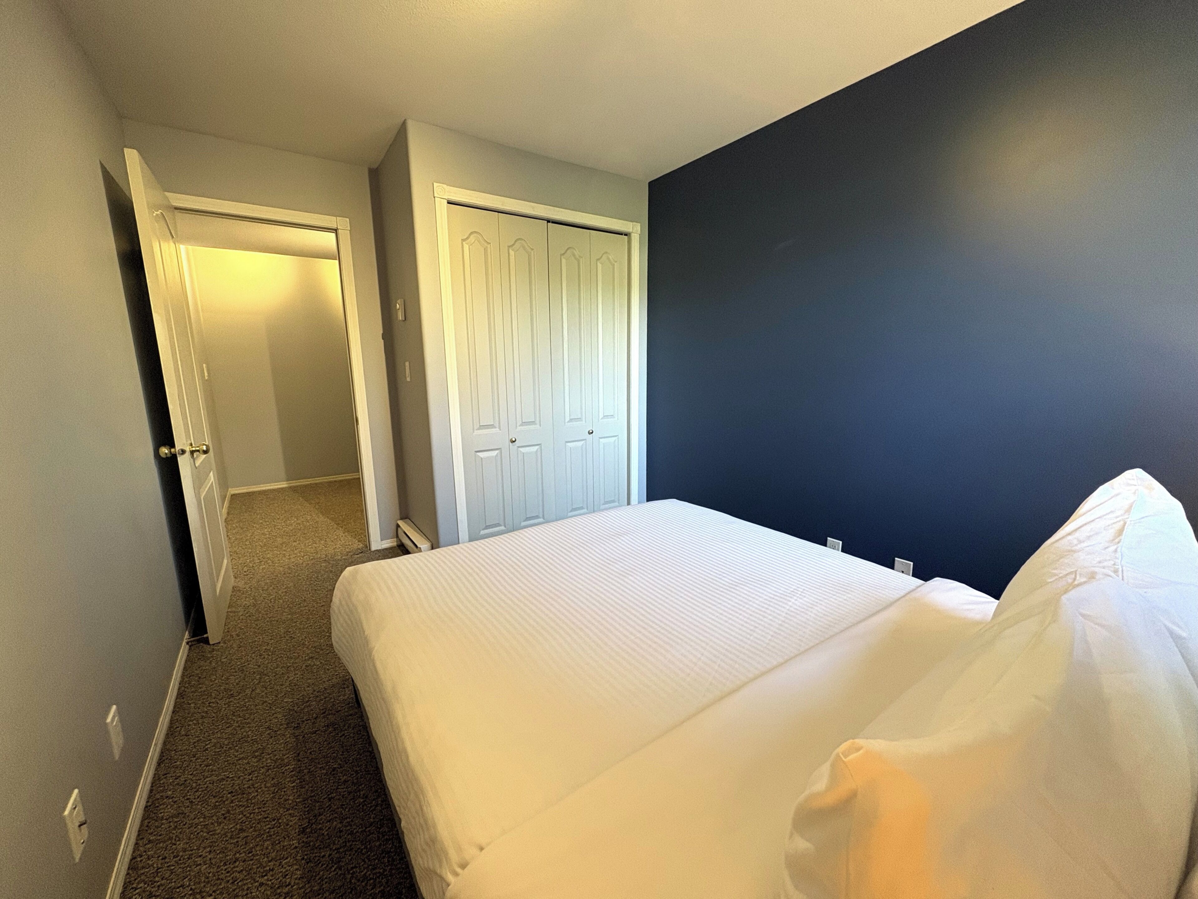 Una habitación de hotel con una cama, una puerta y una pared oscura.