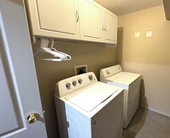 Un lavadero con dos lavadoras y secadoras Whirlpool blancas, una puerta blanca y un interruptor de luz en la pared.