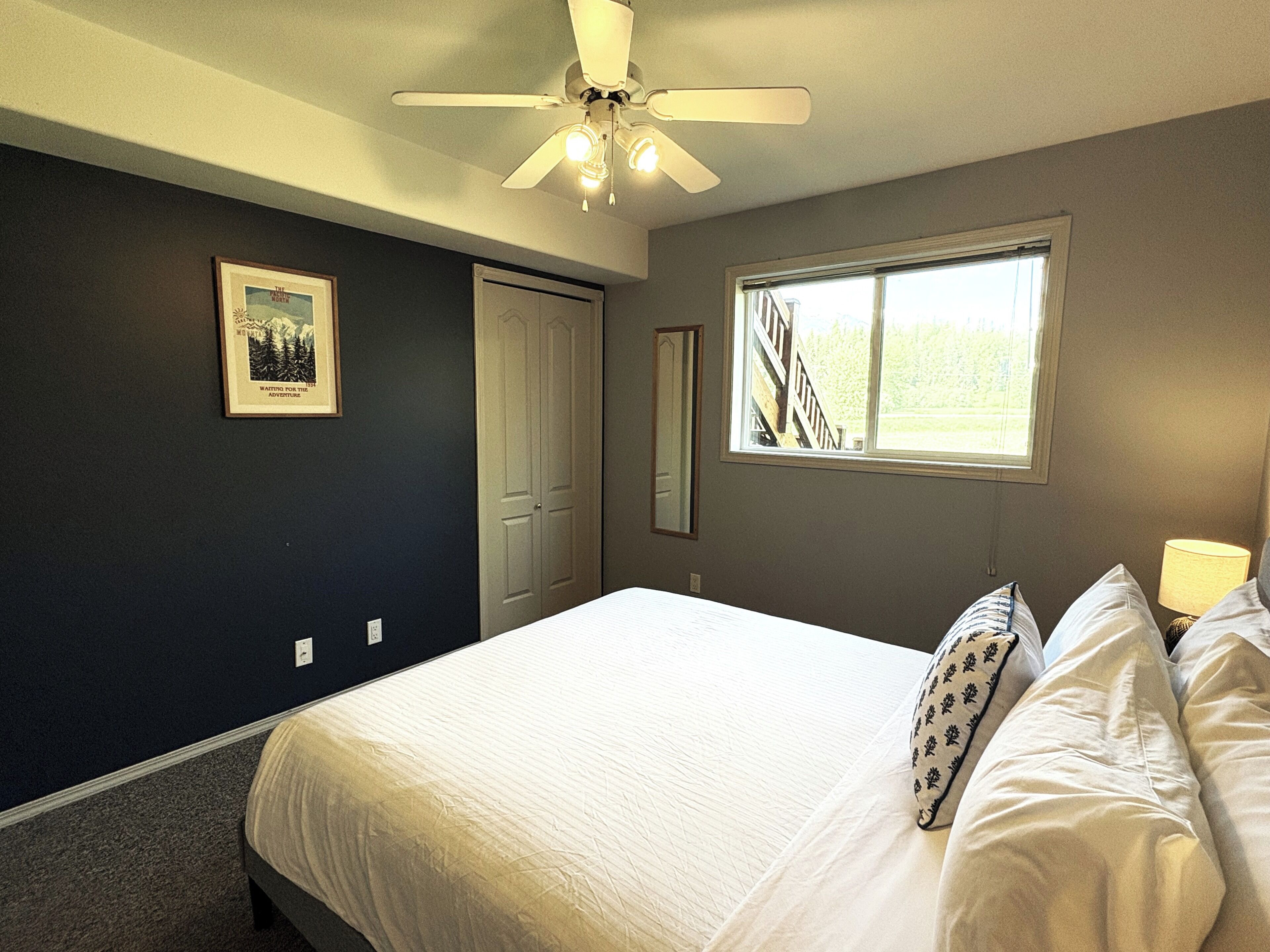A bedroom with a bed, a ceiling fan, a window, and a door.