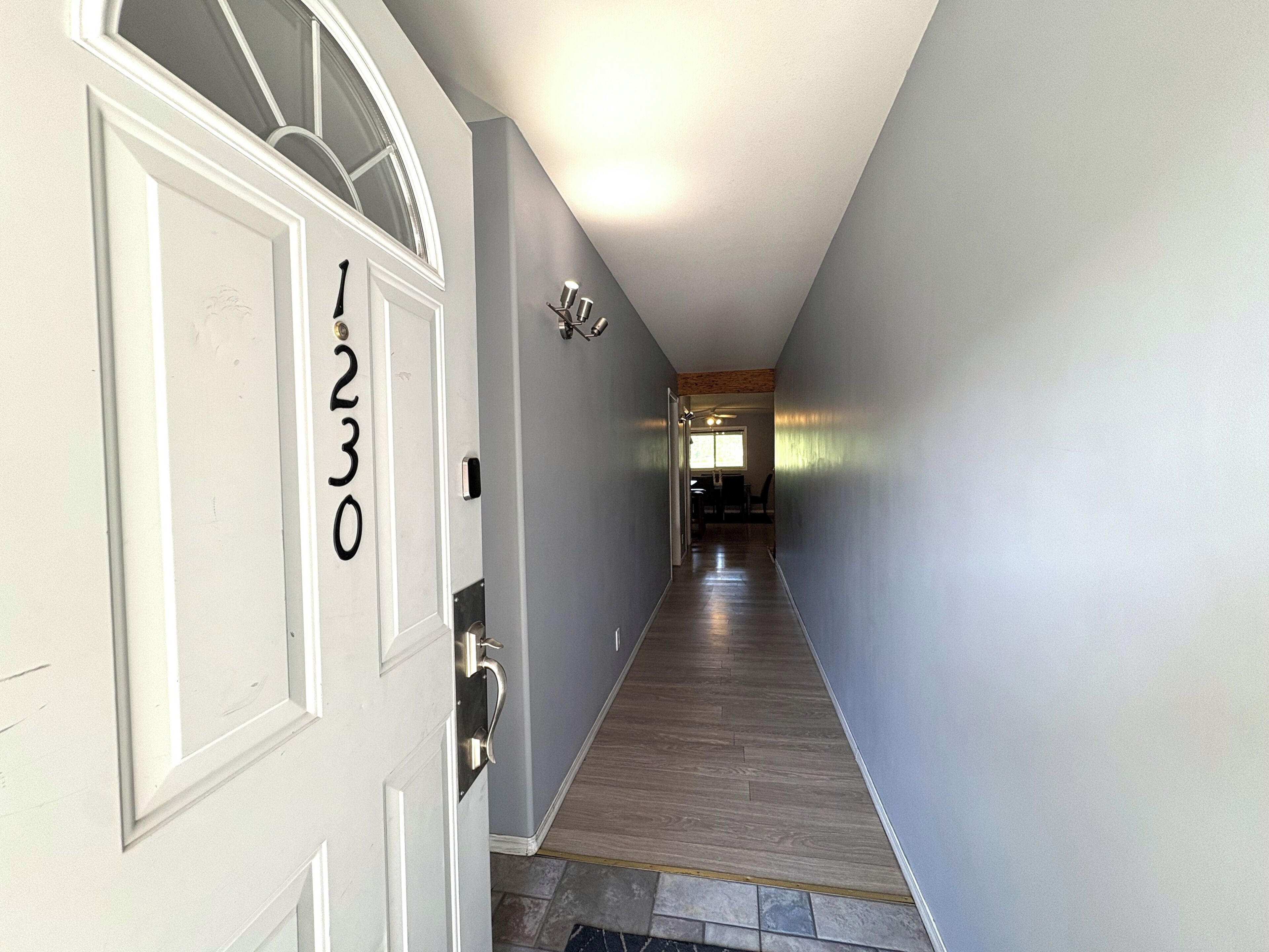 A hallway with a white door marked '1230', a tiled floor, and a dining area in the distance.