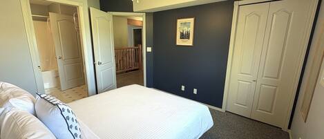 A bedroom with a bed, a ceiling fan, a door, and a framed picture on the wall.