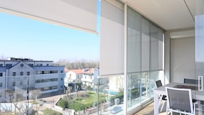 A balcony with a view of a residential area, a table with chairs, and a window with blinds.
