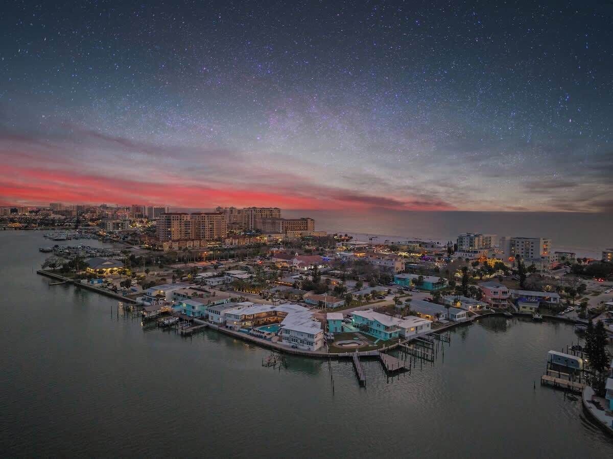 A coastal cityscape at dusk with a marina, buildings, and a starry sky.