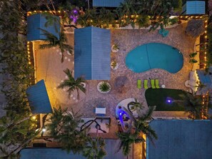 An aerial view of a resort with a swimming pool, lounge areas, and palm trees.