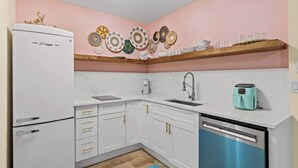 A compact kitchen with white cabinets, a dishwasher, a coffee maker, and a toaster on the countertop.