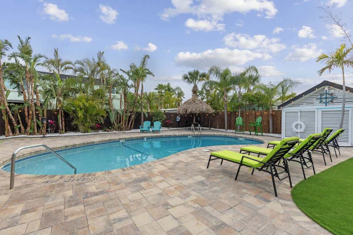 A swimming pool with lounge chairs, palm trees, and a building with a thatched roof.
