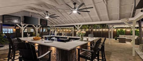 A modern kitchen with a central island, bar stools, ceiling fans, and a dining area with a sofa and chairs.