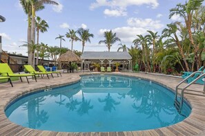 Una piscina con sillas de descanso, palmeras y una zona de estar techada.