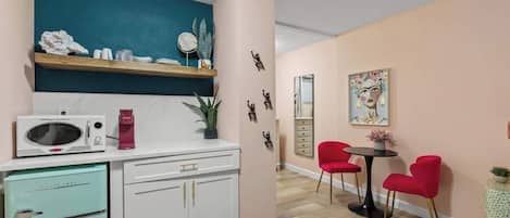 A compact kitchen with a microwave, a vintage refrigerator, and a coffee machine. There is a dining area with a table and red chairs.