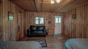 A wooden cabin with a black leather sofa, two checkered beds, and a small table. - Sheriff's Office Cabin At Mountain River Ranch (Ririe)