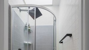 A glass-enclosed shower with white tiled walls and a skylight above.