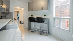 A modern kitchen with white cabinets, a marble countertop, and two black bar stools.