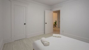 A hotel room with a bed, two doors, and a hallway leading to another room.