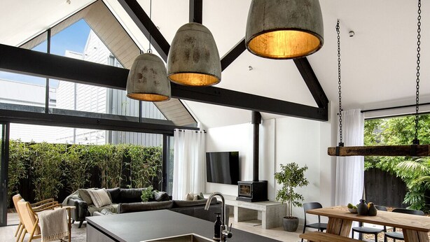 Eine moderne Küche mit einer großen Kochinsel, schwarzen Arbeitsplatten und einer Spüle im Bauernhausstil. Ein Essbereich mit Holztisch und Stühlen sowie eine Sitzecke mit Sofa und Sesseln sind ebenfalls vorhanden.