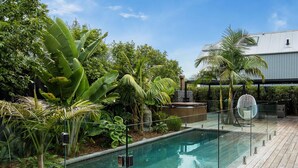 Ein Poolbereich mit Glasabgrenzung, umgeben von tropischen Pflanzen und einem modernen Gebäude im Hintergrund.