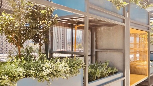 Una estructura arquitectónica moderna con marcos metálicos y paneles de vidrio, que incluye jardines verticales y un área de descanso.