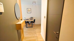 Un pasillo con piso de madera, un escritorio con sillas, un espejo y una puerta.