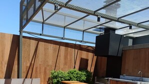 Un área de estar al aire libre con macetas de concreto, mesas de madera y una estación de parrilla metálica.