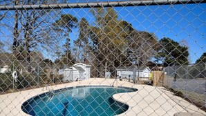 Un patio trasero cercado con piscina, una casa pequeña y una terraza de madera.