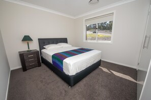 A bedroom with a bed, a nightstand, a lamp, and a window with a view of the outdoors. - Seabreeze at Corlette (Corlette)