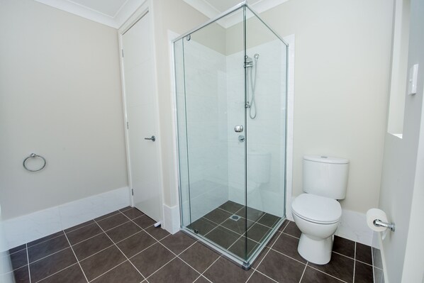 A bathroom with a glass-enclosed shower, a toilet, and a towel ring on the wall. - Seabreeze at Corlette (Corlette)