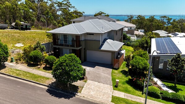 A two-story house with a garage, surrounded by greenery and a view of the sea. - Seabreeze at Corlette (Corlette)