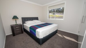 Une chambre à coucher avec un lit, une table de chevet, une lampe et une fenêtre donnant sur l’extérieur.