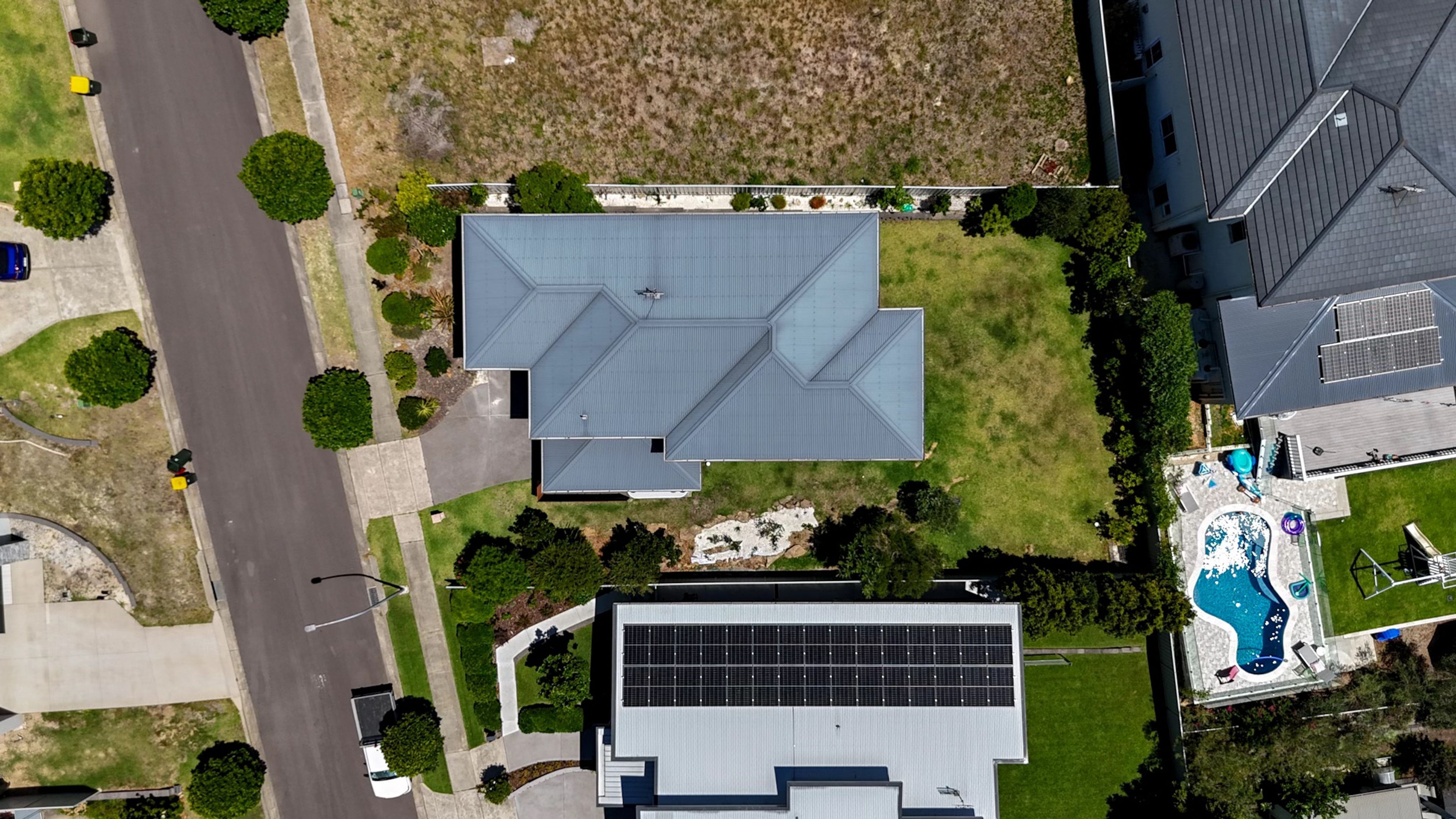 An aerial view of a residential property with a large house, solar panels, a swimming pool, and a well-maintained lawn.