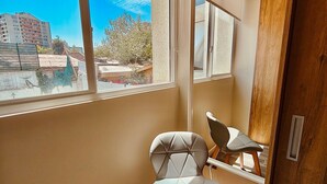 A room with a large window, a chair, and a wooden door. - Confort de Ñuñoa (Santiago)