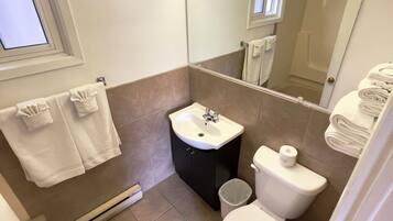 A compact bathroom with a sink, toilet, and mirror. There are towels hanging on the wall and a window above the sink.