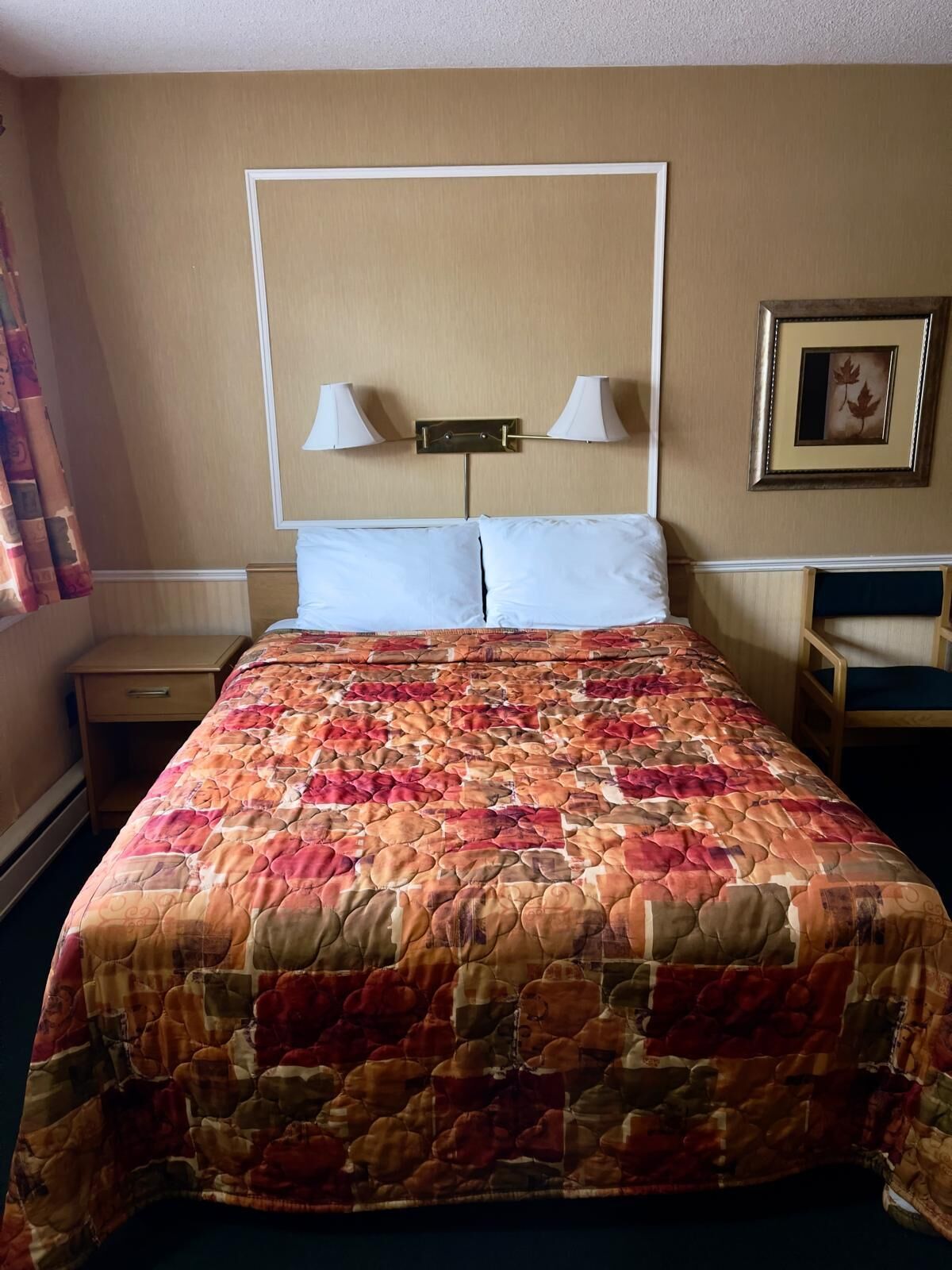 A hotel room with a large bed, two bedside lamps, a nightstand, and a framed picture on the wall.