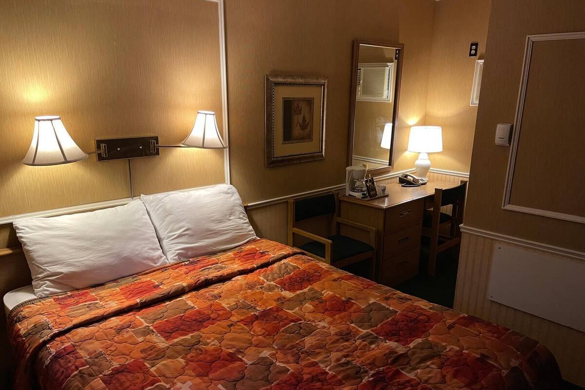 A hotel room with a bed, two bedside lamps, a desk with a chair, a mirror, and a framed picture on the wall.