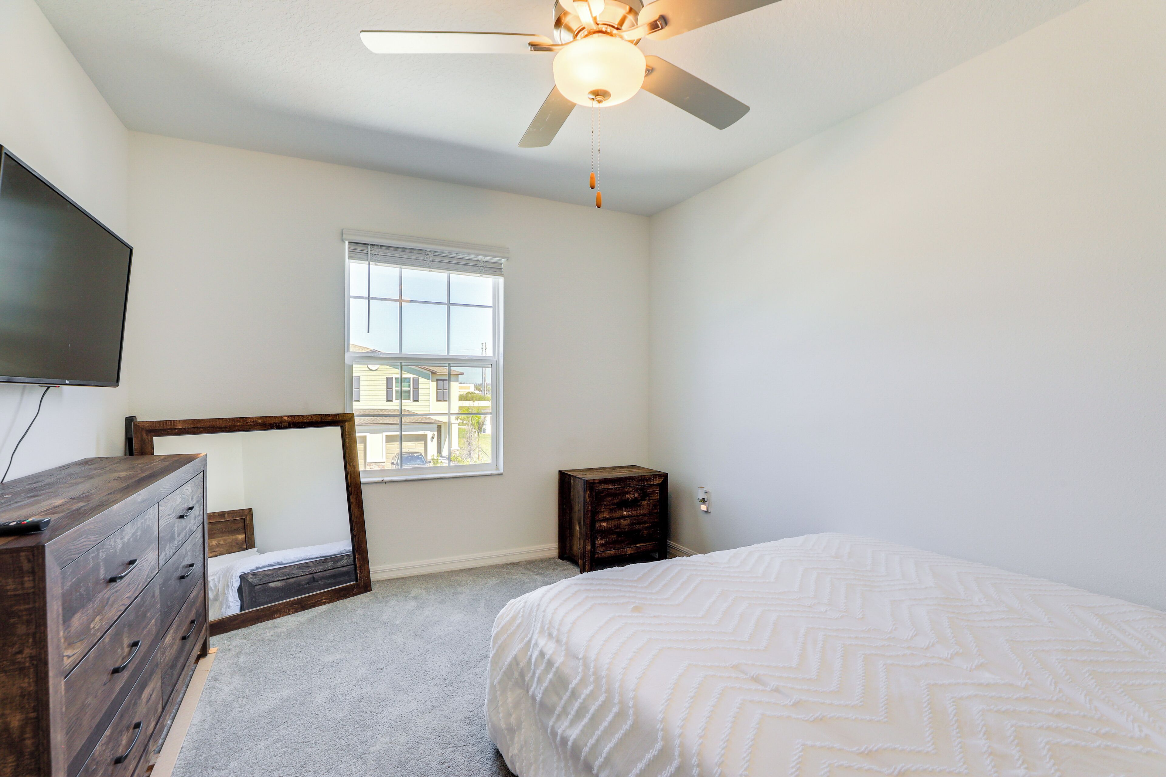 A bedroom with a bed, dresser, vanity mirror, ceiling fan, and window.