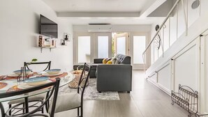 A modern living room with a dining area, a staircase, and a large window. - Modern Beachfront 1BR, 1.5 BATH + Parking (Ocho Rios)