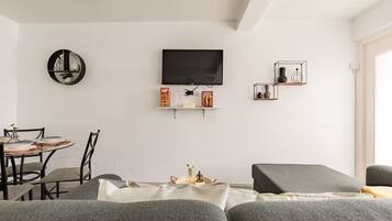 Un salon moderne avec un téléviseur à écran plat, un miroir rond et une table à manger avec des chaises.