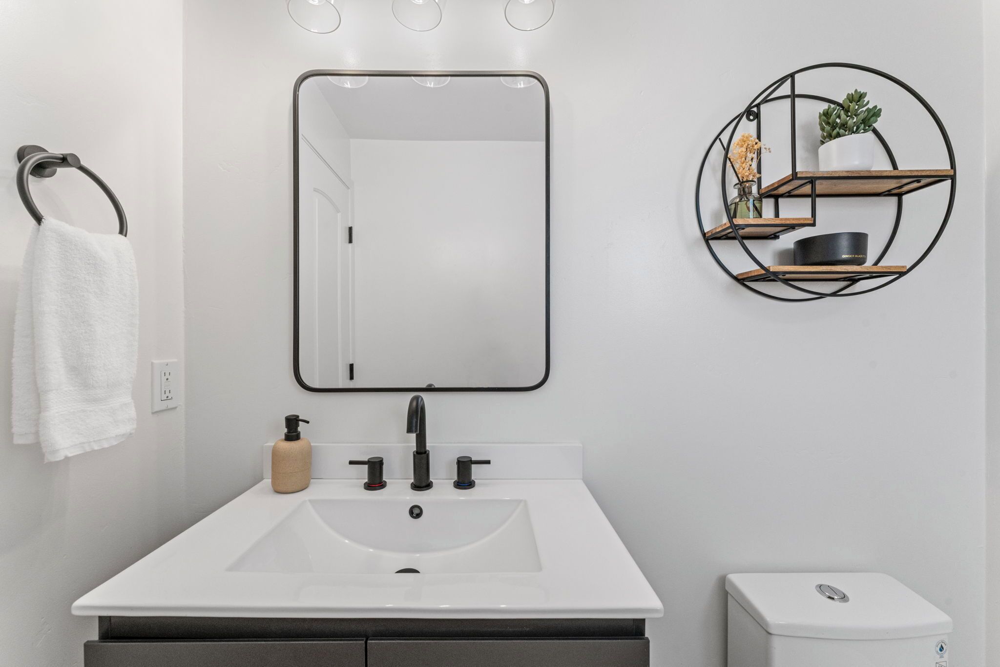 A bathroom with a white sink, black faucet, and a mirror above it. There is a towel rack with a white towel hanging on it.
