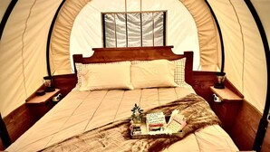 Une pièce aménagée avec une tente, un lit en bois, deux tables de chevet, une fenêtre et un plateau contenant des livres et une plante.