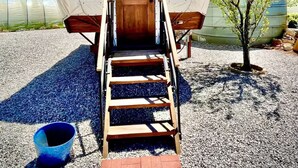 Une structure abritée, dotée d’une porte en bois portant l’inscription « JONES », d’un escalier en bois menant à l’intérieur et d’un petit arbre situé à proximité.