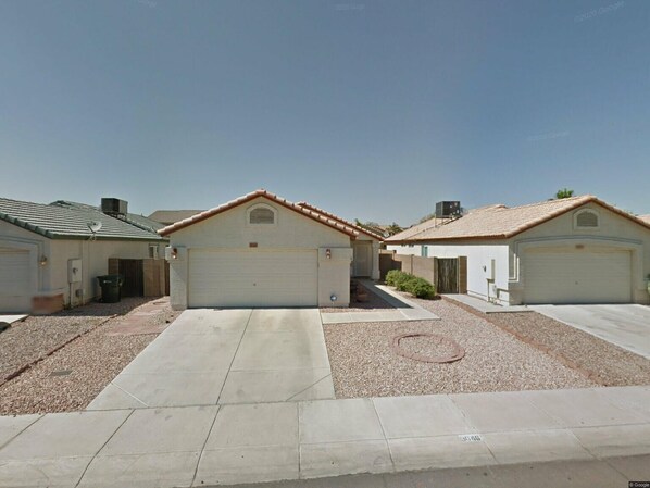 A residential area with three single-story houses, each with a garage, a small front yard, and a clear sky.