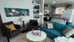 En moderne stue med et rundt sofabord, to sofaer, en bogreol og et køkken i baggrunden.