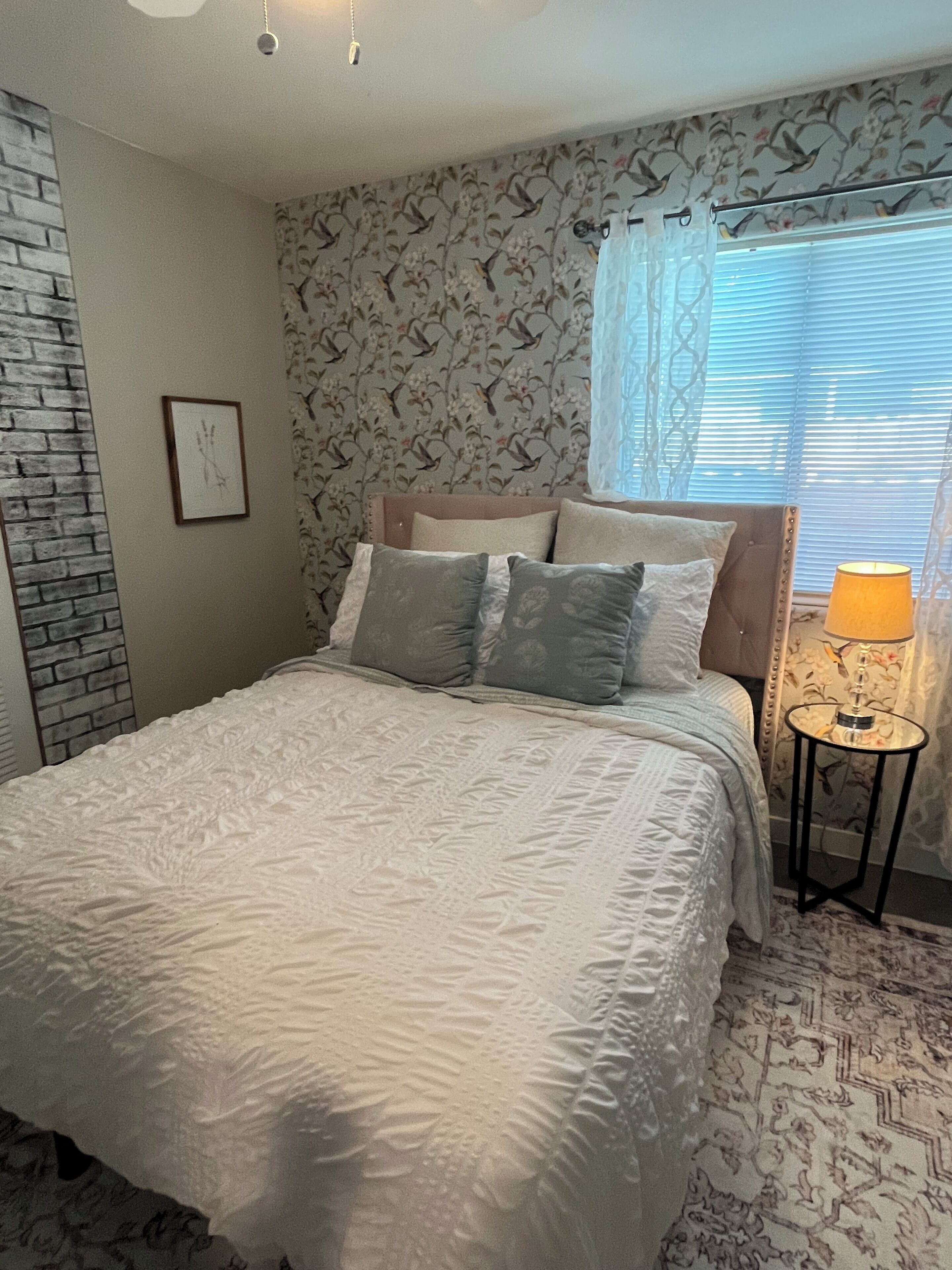 A bedroom with a bed, a nightstand, a lamp, and a window with blinds.