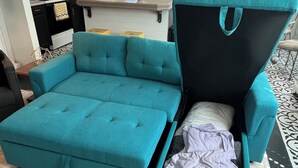 En turkis modulsofa med sovemulighed, et køkken med hvide skabe, en mikrobølgeovn og en hængende lampe.