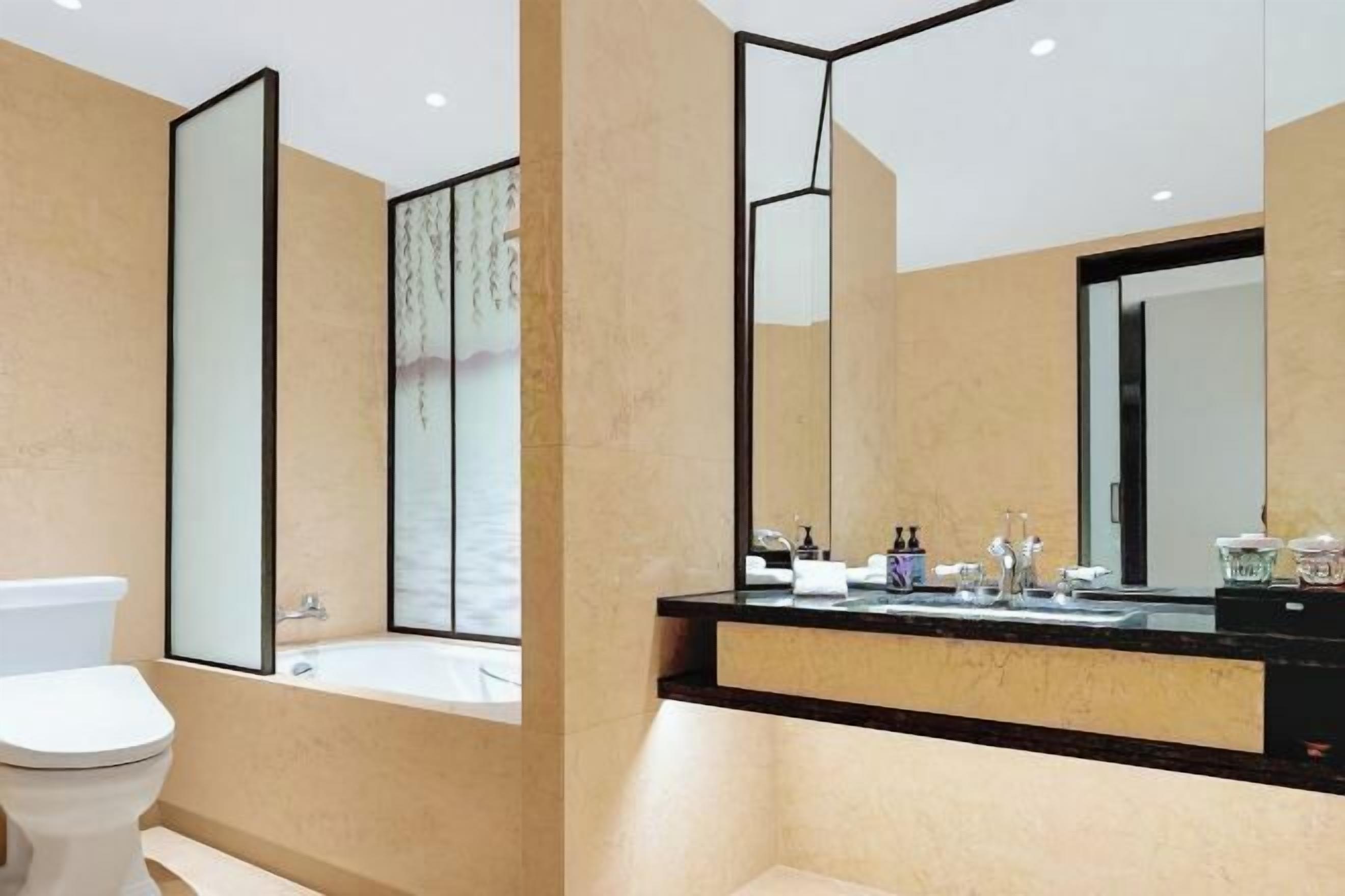Une salle de bain moderne équipée de toilettes, d’une baignoire et d’un grand miroir.
